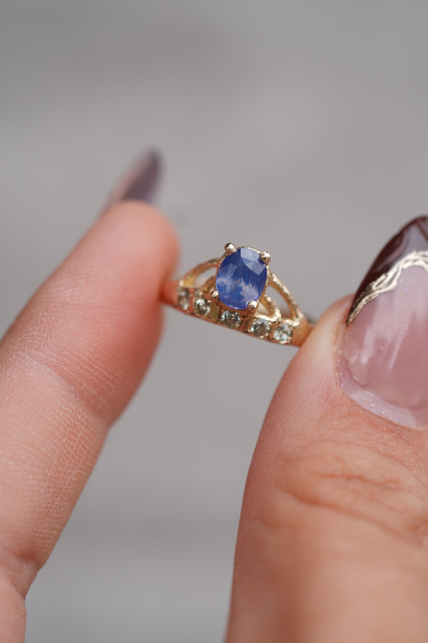 Gold ring with a blue gemstone held between fingers against a blurred background