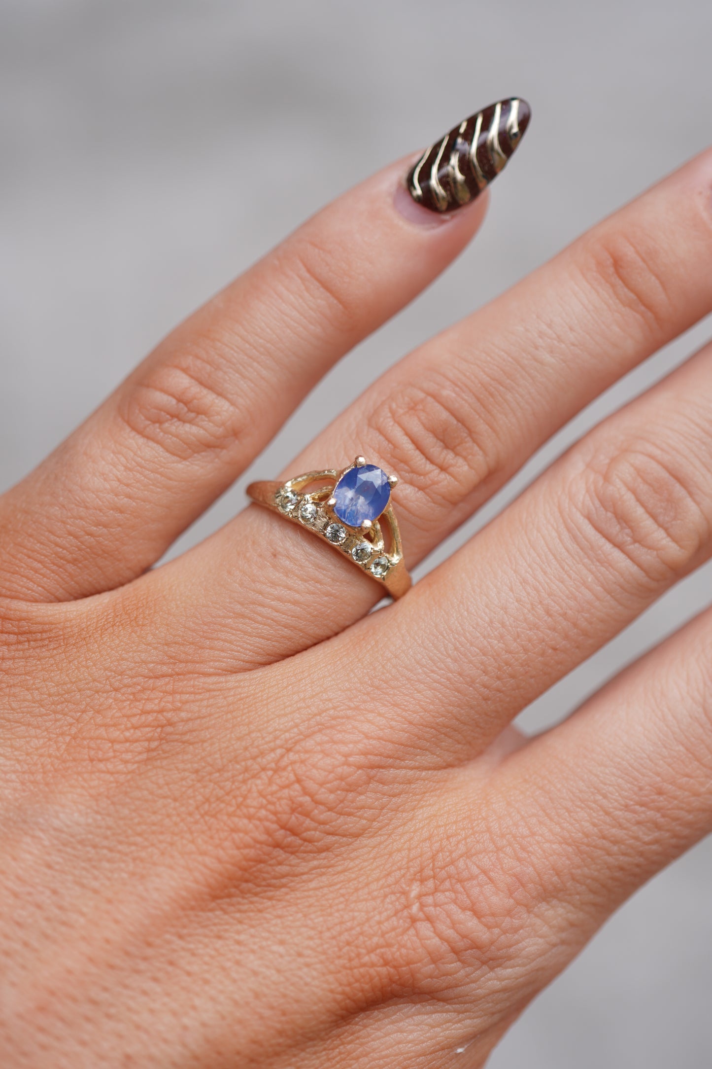Hand wearing a ring with a blue gemstone on a neutral background