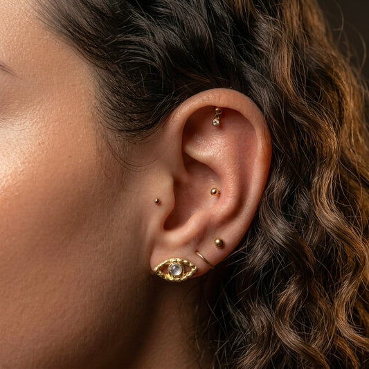 Close-up of an ear with gold earrings and dark hair.