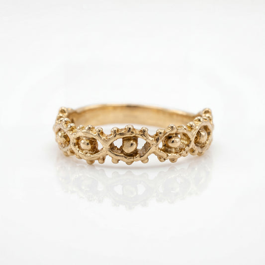 Gold ring with intricate eye design on a white background