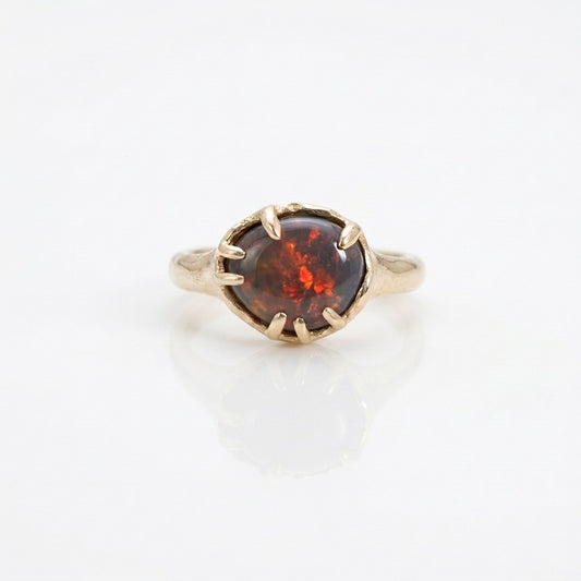 Gold ring with a red flashing opal on a white background